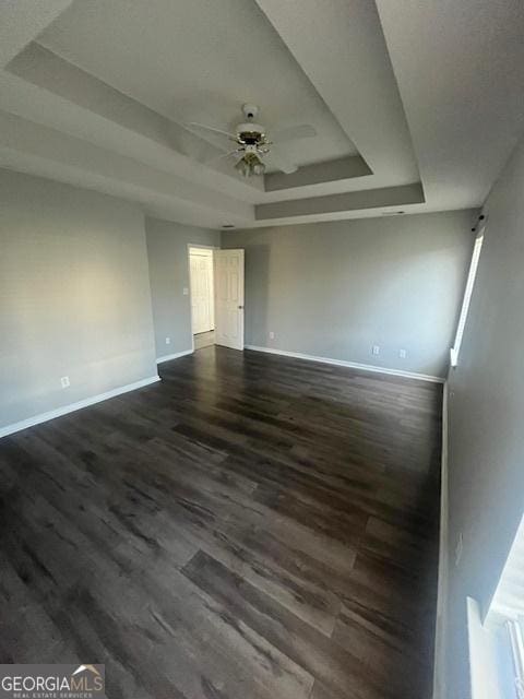 empty room featuring a raised ceiling, ceiling fan, and dark wood-type flooring