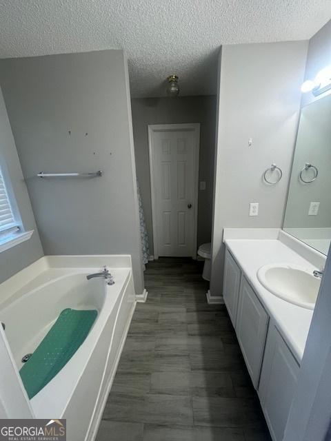 bathroom featuring a washtub, vanity, a textured ceiling, and toilet