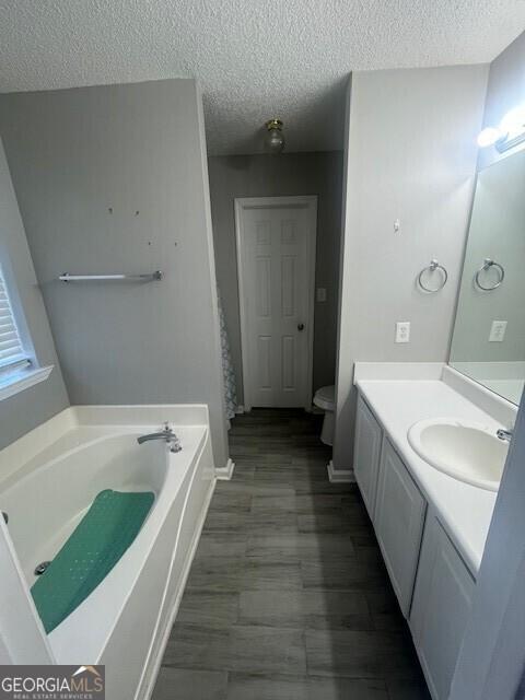 bathroom featuring vanity, a bath, a textured ceiling, and toilet