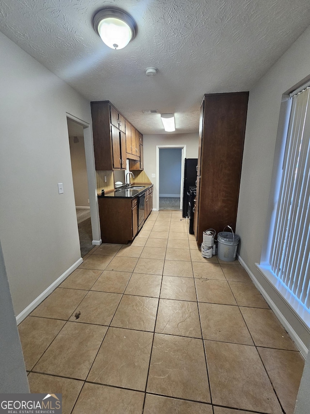 kitchen featuring refrigerator, sink, light tile patterned floors, a textured ceiling, and black dishwasher