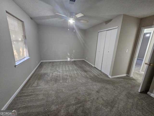 unfurnished bedroom with ceiling fan, a closet, a textured ceiling, and dark colored carpet