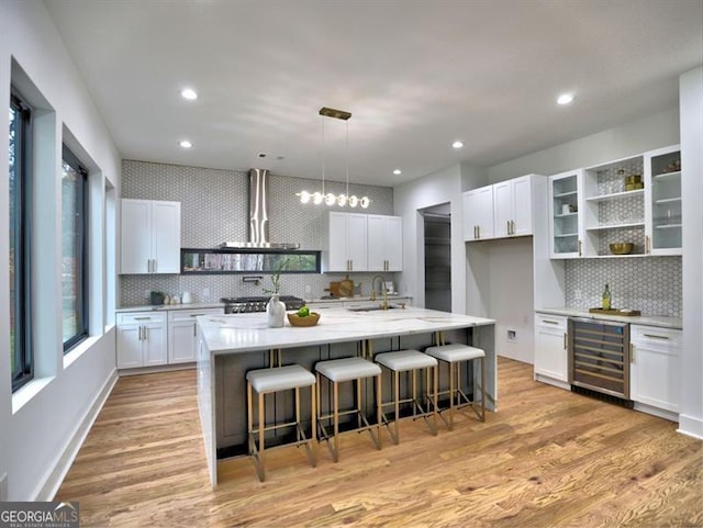 kitchen with light wood-type flooring, white cabinets, wine cooler, a breakfast bar area, and an island with sink