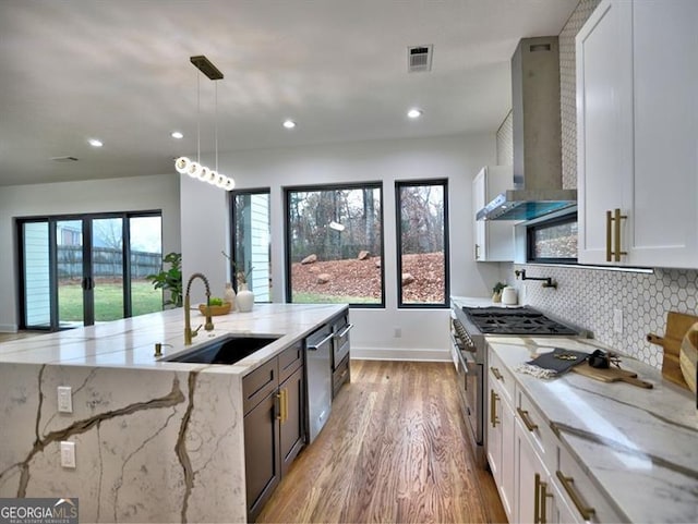 kitchen featuring light stone countertops, pendant lighting, white cabinetry, and wall chimney range hood