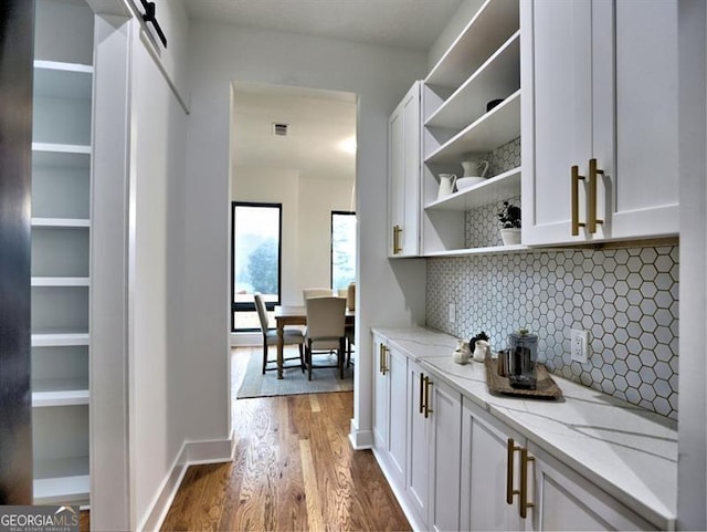 bar featuring light stone countertops, tasteful backsplash, a barn door, hardwood / wood-style floors, and white cabinets