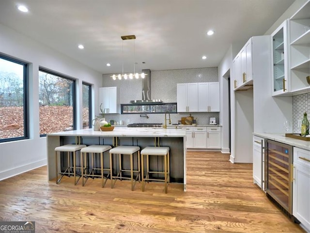 kitchen featuring wine cooler, light hardwood / wood-style floors, decorative light fixtures, a kitchen island with sink, and white cabinets