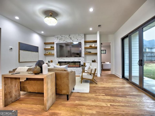 living room featuring light wood-type flooring, a fireplace, a wealth of natural light, and french doors