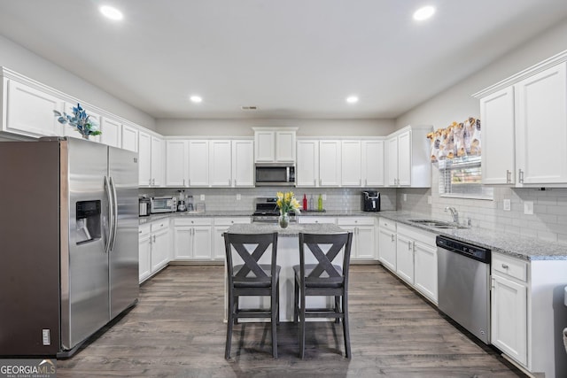 kitchen featuring white cabinets, stainless steel appliances, a kitchen island, and light stone counters