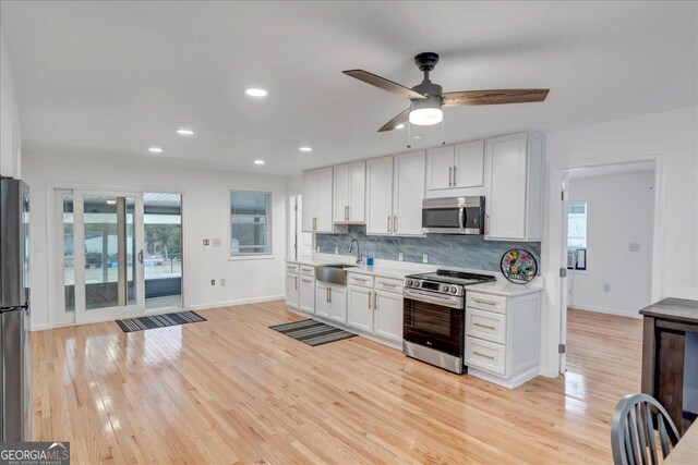 kitchen with white cabinetry, sink, ceiling fan, stainless steel appliances, and light hardwood / wood-style floors