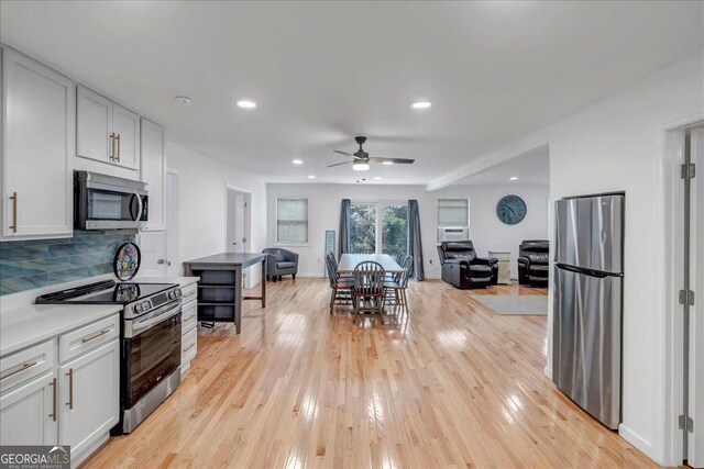 kitchen featuring backsplash, white cabinets, ceiling fan, light wood-type flooring, and appliances with stainless steel finishes