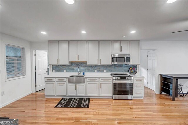 kitchen featuring light wood-type flooring, sink, appliances with stainless steel finishes, and tasteful backsplash