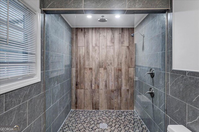 bathroom with toilet, a tile shower, and tile walls