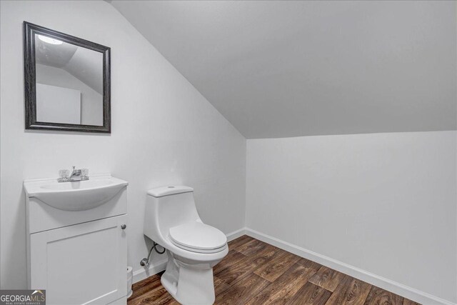 bathroom featuring hardwood / wood-style flooring, vanity, toilet, and vaulted ceiling