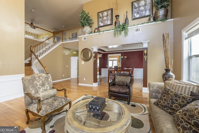 living room with hardwood / wood-style floors, plenty of natural light, ornate columns, and a towering ceiling