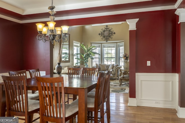 dining space featuring hardwood / wood-style floors, a notable chandelier, ornamental molding, and ornate columns