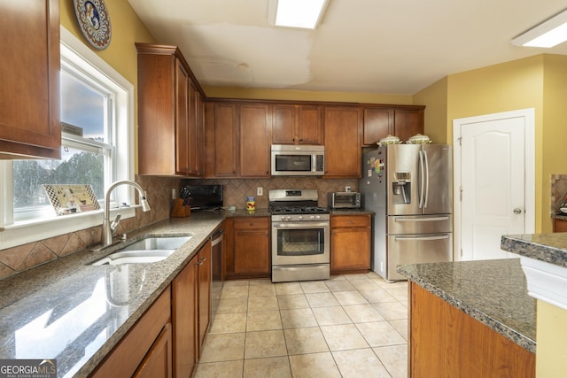 kitchen featuring decorative backsplash, dark stone counters, stainless steel appliances, sink, and light tile patterned flooring