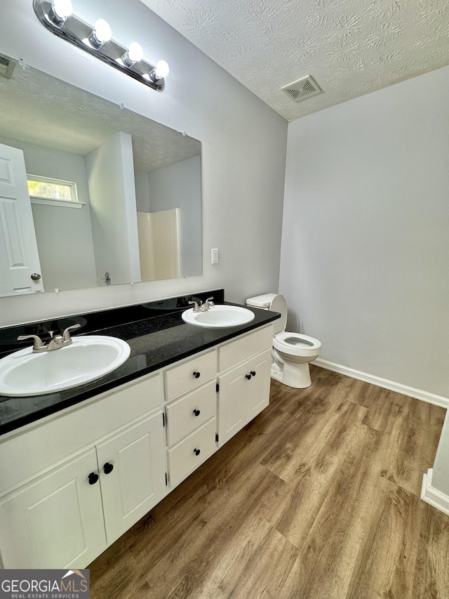 bathroom featuring vanity, a shower, hardwood / wood-style flooring, toilet, and a textured ceiling