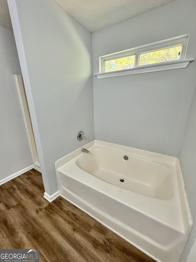 bathroom featuring plenty of natural light, a bathtub, wood-type flooring, and a textured ceiling