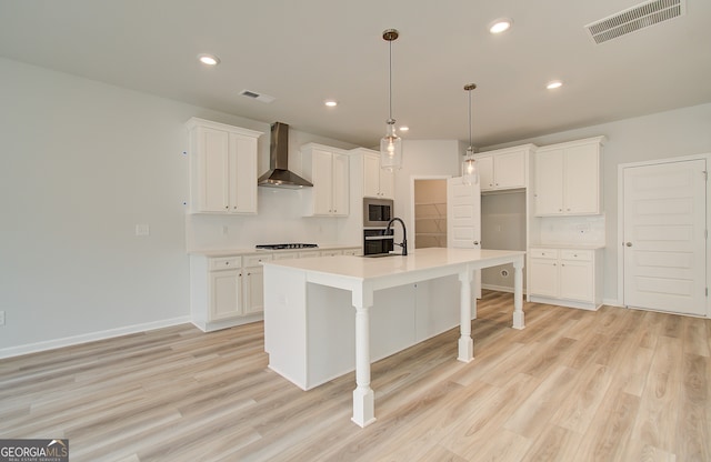 kitchen featuring stainless steel microwave, an island with sink, white cabinets, and wall chimney range hood