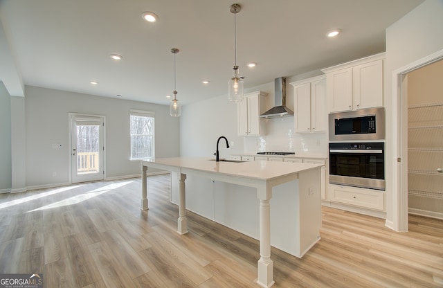 kitchen with sink, white cabinetry, an island with sink, stainless steel appliances, and wall chimney exhaust hood