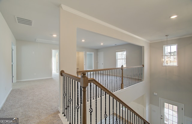 corridor with a wealth of natural light, ornamental molding, light carpet, and a notable chandelier