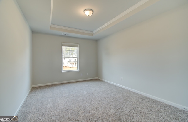 empty room featuring a tray ceiling, ornamental molding, and carpet flooring