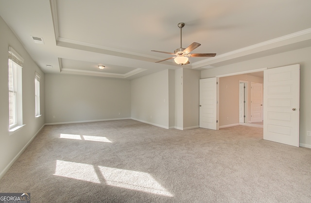 carpeted spare room featuring ceiling fan, ornamental molding, a raised ceiling, and a healthy amount of sunlight