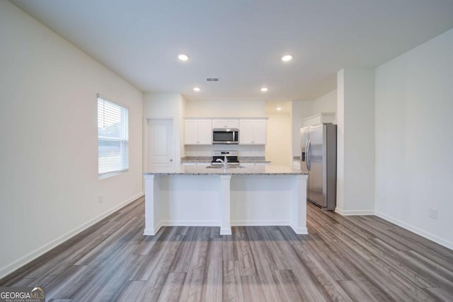 kitchen featuring white cabinets, appliances with stainless steel finishes, light stone countertops, and wood-type flooring