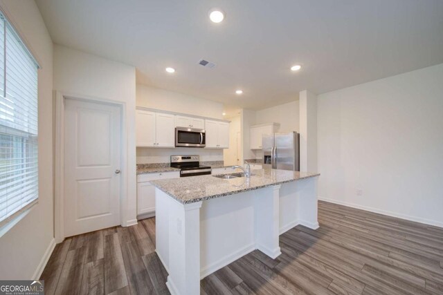 kitchen with light stone countertops, appliances with stainless steel finishes, a kitchen island with sink, white cabinets, and light hardwood / wood-style floors