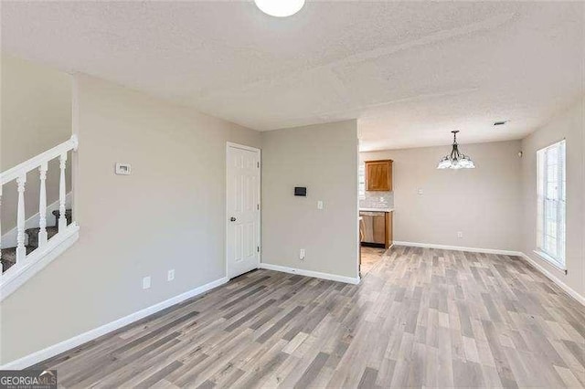 unfurnished living room featuring a chandelier, hardwood / wood-style floors, and a textured ceiling