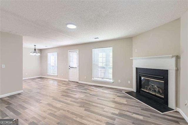 unfurnished living room with a textured ceiling, hardwood / wood-style flooring, and a notable chandelier