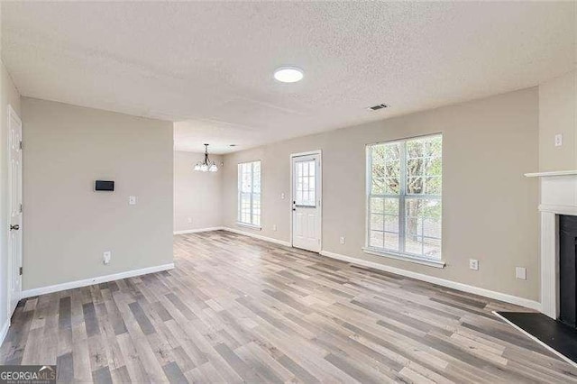 unfurnished living room featuring a textured ceiling, light hardwood / wood-style floors, and an inviting chandelier