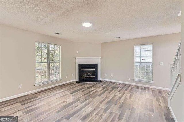 unfurnished living room featuring a wealth of natural light, light hardwood / wood-style floors, and a textured ceiling