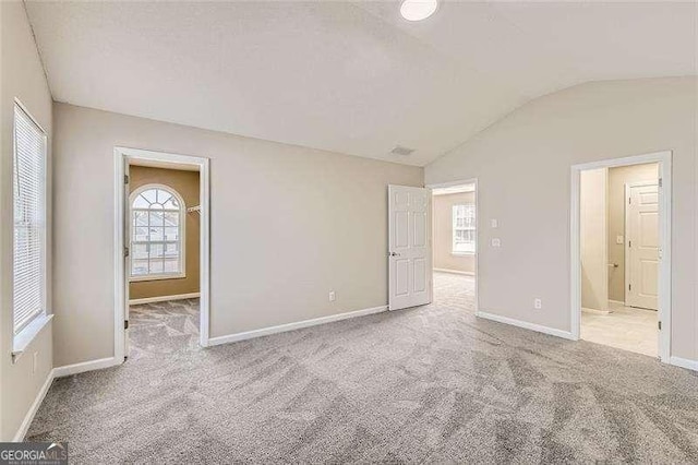 unfurnished bedroom with connected bathroom, light colored carpet, and vaulted ceiling