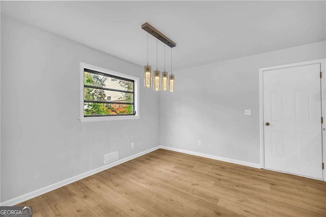 empty room featuring light wood-type flooring and a notable chandelier