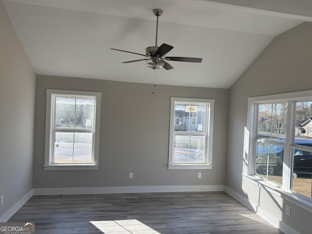 unfurnished room featuring a wealth of natural light, wood finished floors, baseboards, and vaulted ceiling