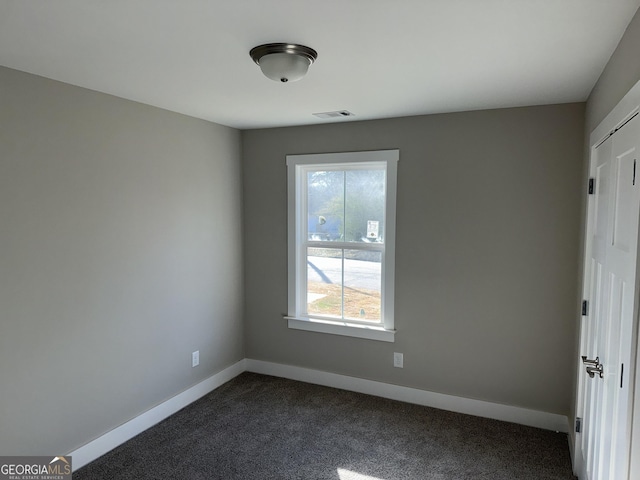 spare room with visible vents, baseboards, and dark carpet