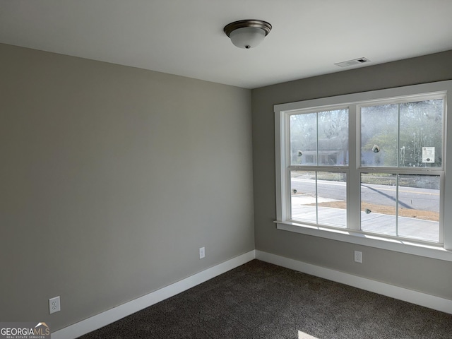 spare room featuring visible vents, baseboards, and dark carpet