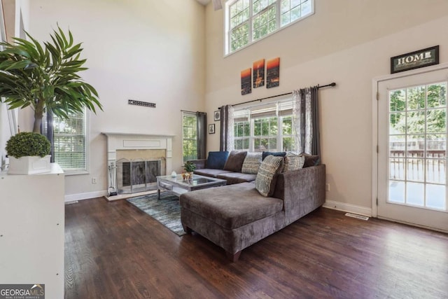 living room with dark hardwood / wood-style flooring, a premium fireplace, and a towering ceiling