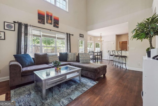 living room with dark hardwood / wood-style floors, a healthy amount of sunlight, a towering ceiling, and an inviting chandelier