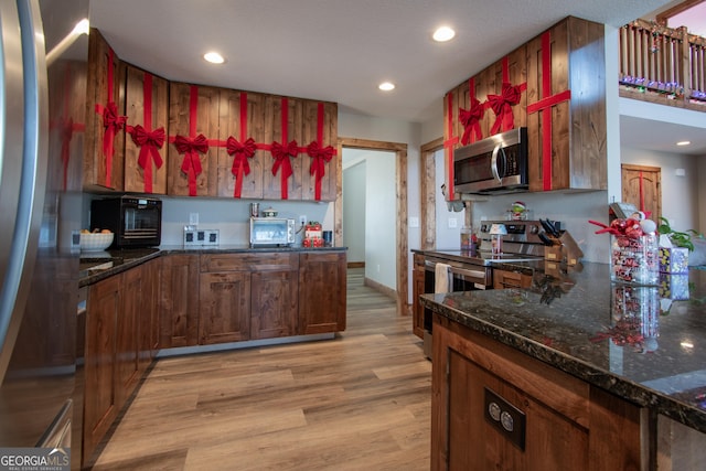 kitchen featuring dark stone countertops, light wood-type flooring, and appliances with stainless steel finishes