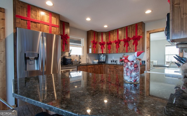 kitchen with sink, stainless steel appliances, a wealth of natural light, and dark stone countertops