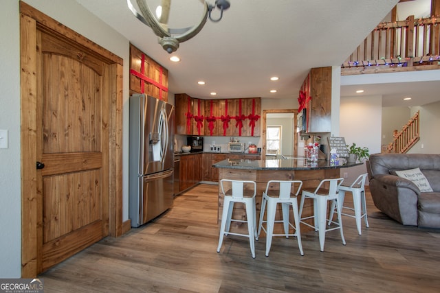 kitchen with kitchen peninsula, appliances with stainless steel finishes, a kitchen bar, hardwood / wood-style flooring, and an inviting chandelier