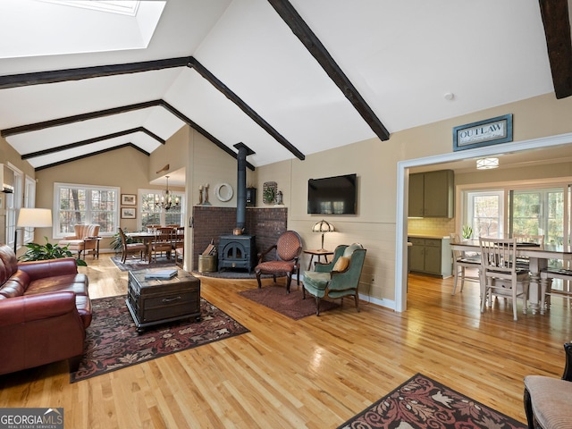 living room featuring a wood stove, high vaulted ceiling, beam ceiling, light hardwood / wood-style floors, and a chandelier