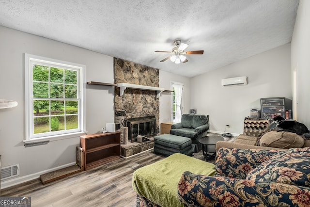 living room featuring a wall mounted air conditioner, a stone fireplace, vaulted ceiling, light hardwood / wood-style flooring, and a textured ceiling