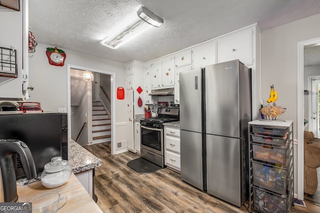 kitchen featuring light stone counters, a textured ceiling, stainless steel appliances, white cabinets, and dark hardwood / wood-style floors