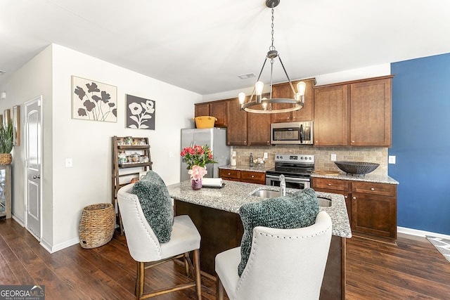 kitchen featuring a kitchen island with sink, dark wood-type flooring, decorative light fixtures, decorative backsplash, and appliances with stainless steel finishes