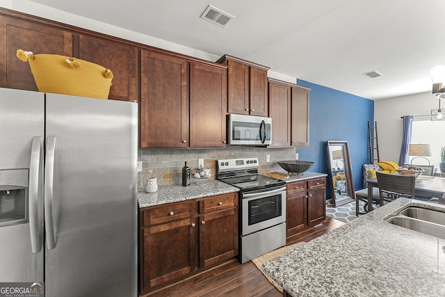 kitchen featuring light stone countertops, sink, dark wood-type flooring, stainless steel appliances, and decorative backsplash