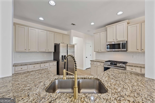 kitchen with sink, stainless steel appliances, light stone counters, light hardwood / wood-style flooring, and backsplash