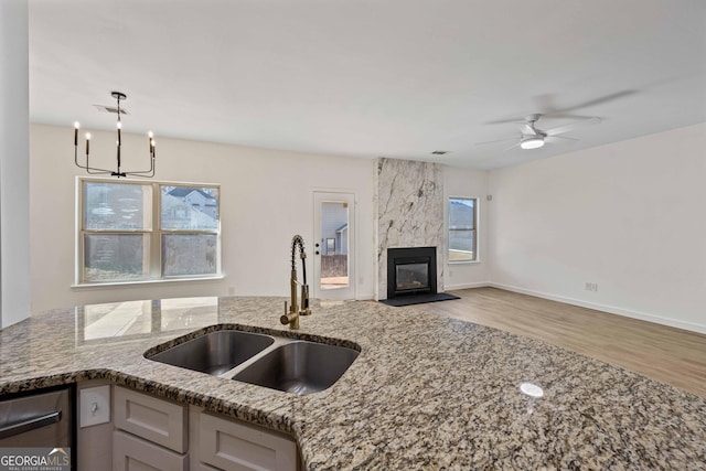 kitchen with light stone countertops, a high end fireplace, stainless steel dishwasher, sink, and light hardwood / wood-style flooring