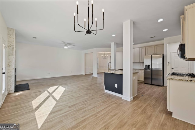 kitchen with appliances with stainless steel finishes, light stone counters, ceiling fan, cream cabinets, and light hardwood / wood-style flooring